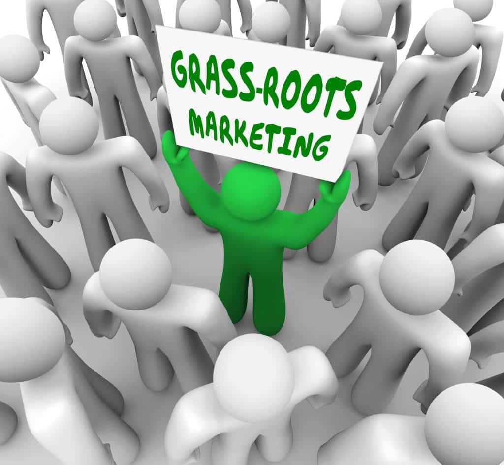 A green figure standing in a crowd of others holding a sign that says "Grass Roots Marketing"